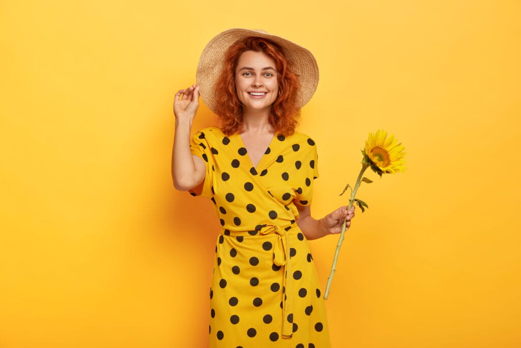Summer portrait smiling mirthful ginger lady with tender smile stands with sunflower picked from field